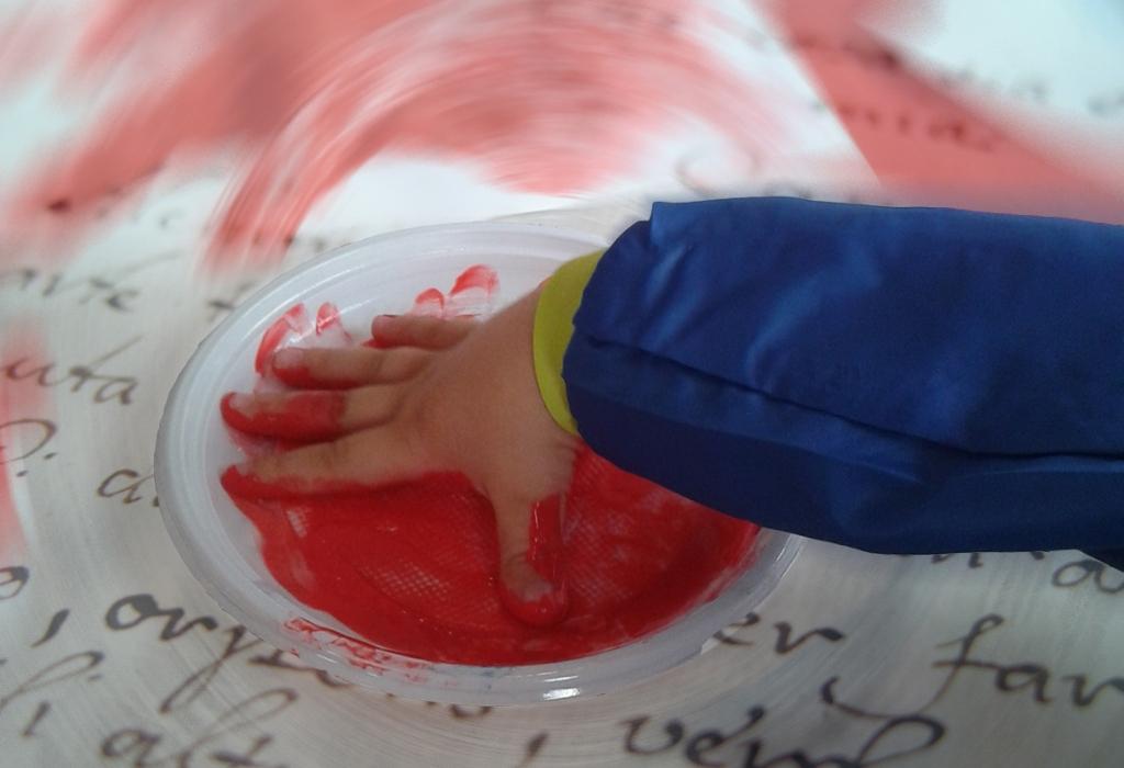 fotografia della manina di un bambino su un piatto pieno di tempera rossa, sfondo con sfocatura radiale